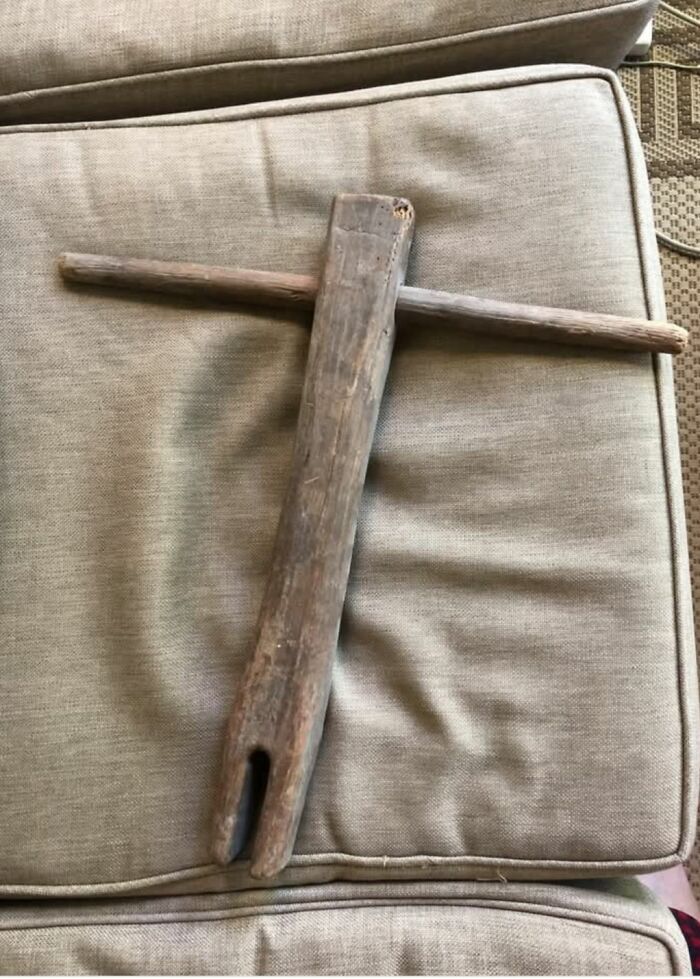 Old wooden tool resembling a strange artifact found in homes with hidden or haunted pasts resting on beige cushions.