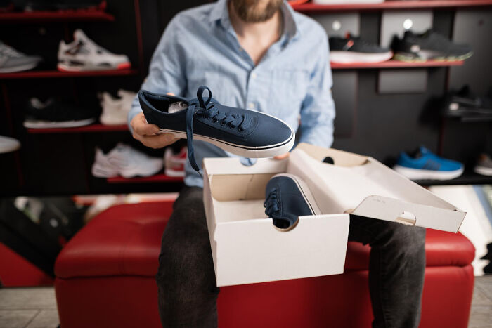 Person holding a sneaker from a box in a shoe store, illustrating everyday items that have become stupid expensive.