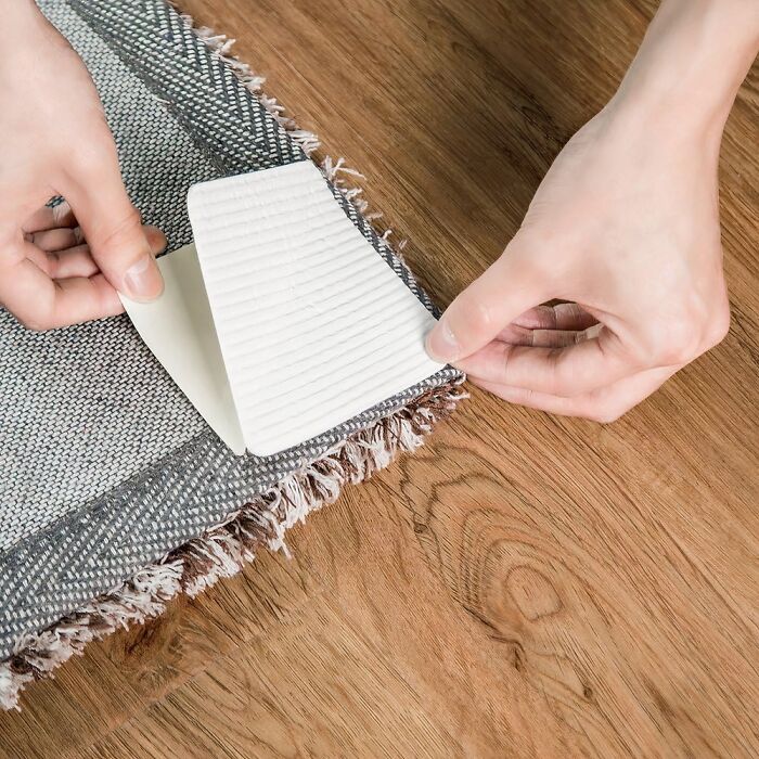 Hands applying an anti-slip pad under a rug to prevent everyday annoyances with home finds under $20.
