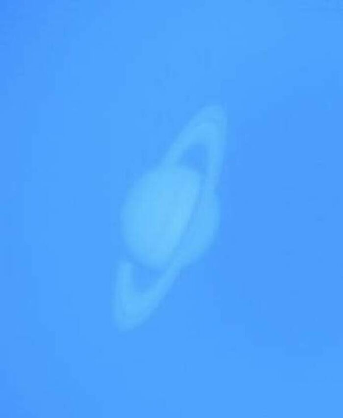 Faint alternate angle of Saturn captured against a clear blue sky, showing its iconic rings in soft focus.