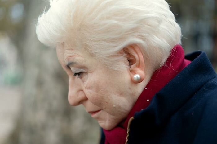 Close-up of a hyper-realistic sculpture by Ruben Orozco Loza showing an elderly woman with white hair and pearl earrings.