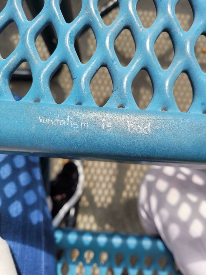 Close-up of blue metal bench with small handwritten chalk message about vandalism reflecting wholesome street vandal acts.