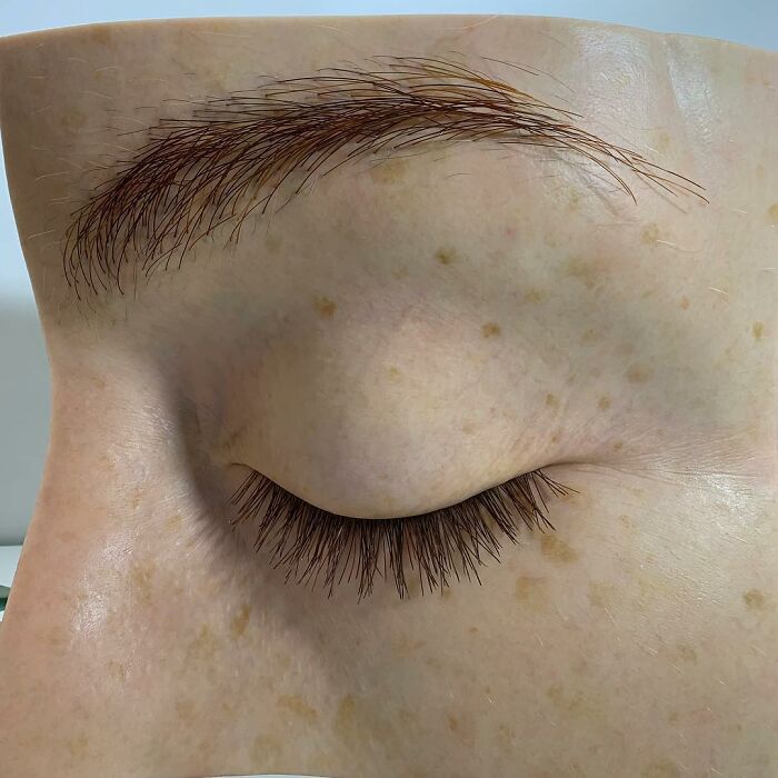 Close-up of a hyper-realistic sculpture eye with detailed eyelashes and eyebrow by Ruben Orozco Loza.