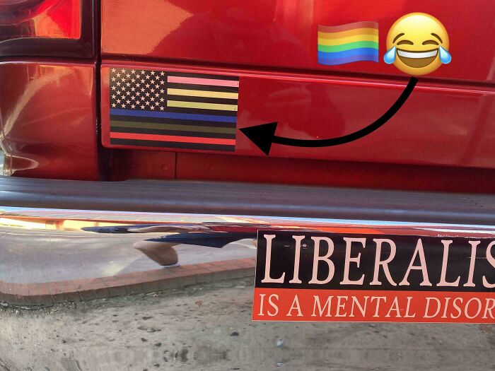 Red vehicle with a humorous sticker alteration showing a modified flag as an example of wholesome street vandalism.