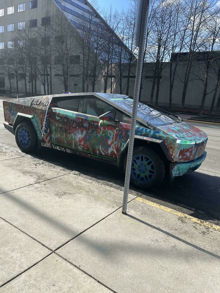 Graffiti-covered Cybertruck parked on a city street, showcasing wholesome vandals' art improving urban surroundings.