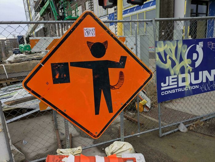 Street sign creatively altered with cat ears and tail graffiti, showcasing wholesome vandalism that improves urban appearance.