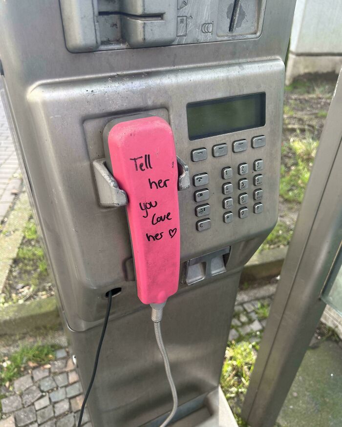 Public phone with a pink handset featuring a wholesome message, showcasing creative street wholesome vandalism.
