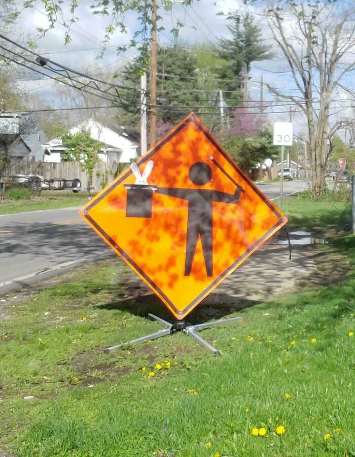 Street sign creatively altered to show a person pulling a rabbit from a hat, a wholesome vandalism enhancing urban streetscapes.