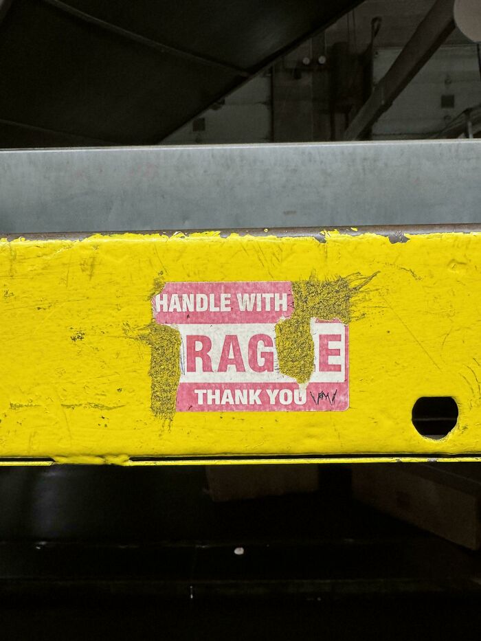 Worn yellow metal surface with partially peeled sticker showing the word rage, capturing wholesome vandalism on streets.