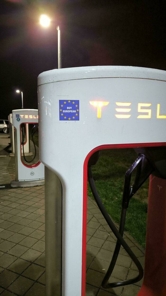 Tesla electric car charging station at night with a Buy European sticker, showcasing wholesome vandalism on streets.