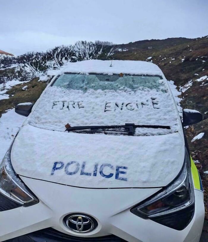Police car covered in snow with the words fire engine carved on the windshield, wholesome vandalism on streets.
