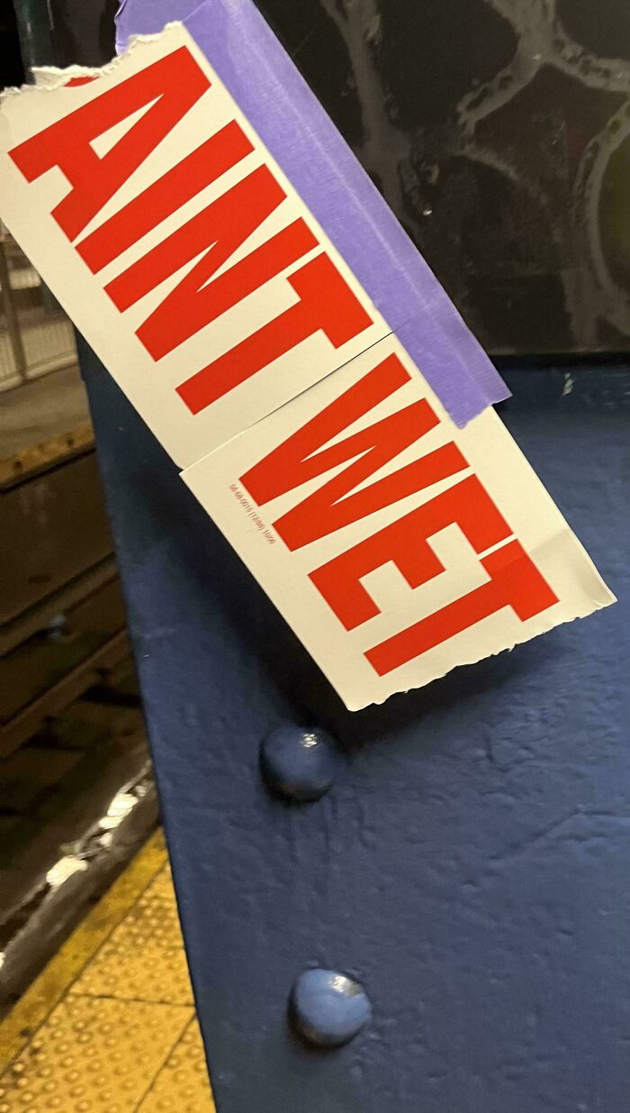 Sticker with bold red letters taped to a blue street surface, showcasing creative wholesome vandalism on urban streets.