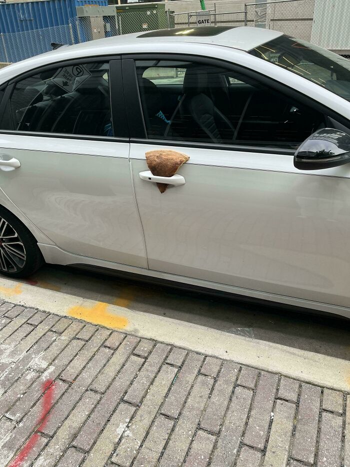 White car with a creative wholesome vandalism repair on the door handle using a woven basket piece outdoors.