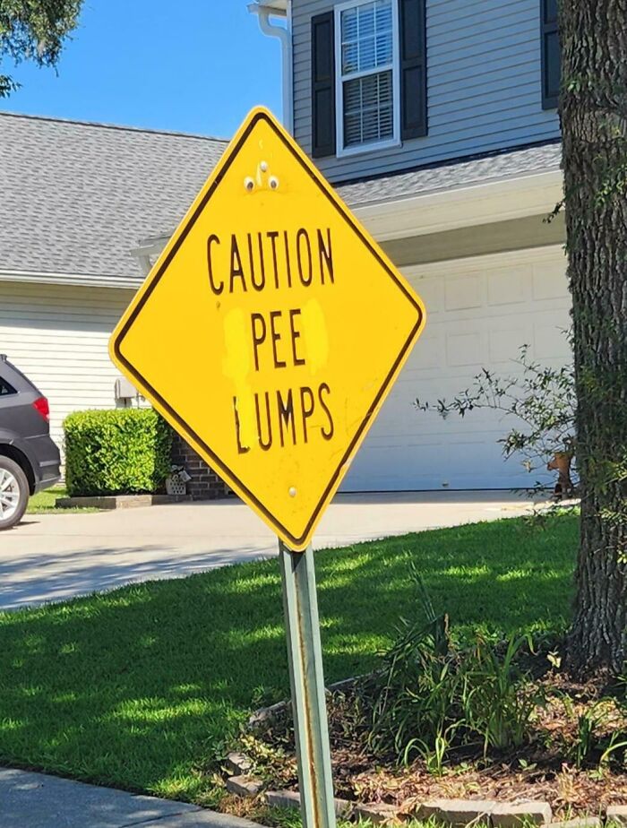 Yellow street sign humorously altered by wholesome vandals to read "Caution Pee Lumps" in a suburban neighborhood setting.