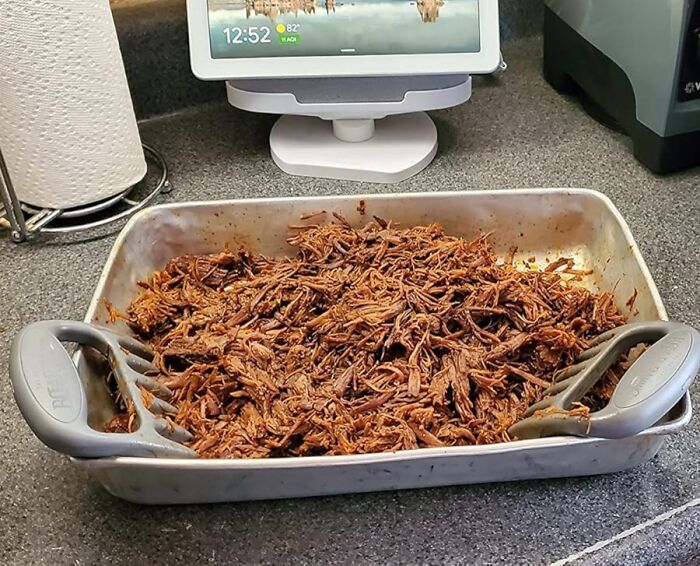 Shredded meat being pulled apart with smart kitchen gadgets on a countertop beside a digital assistant display.