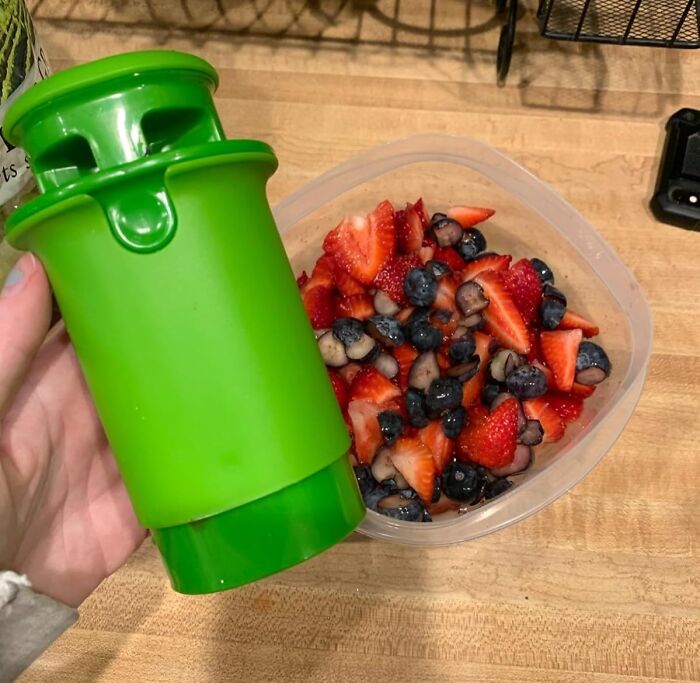 Green smart kitchen gadget held over a container of chopped strawberries and blueberries on a wooden countertop.