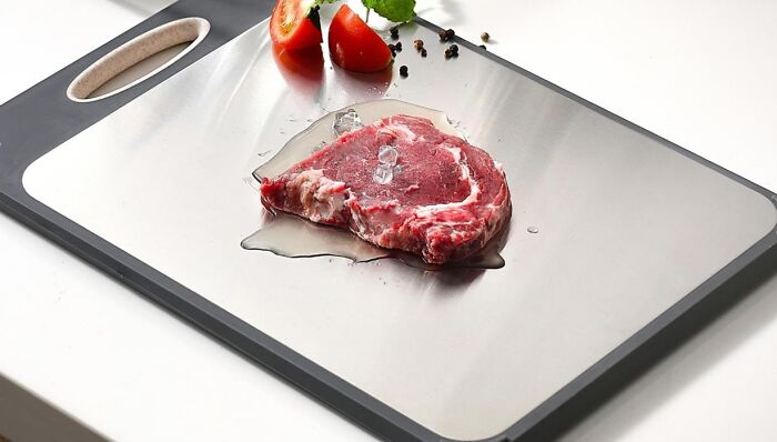 Metal kitchen cutting board with fresh steak, ice cubes, tomato slices, and peppercorns showcasing smart gadgets for kitchen use.