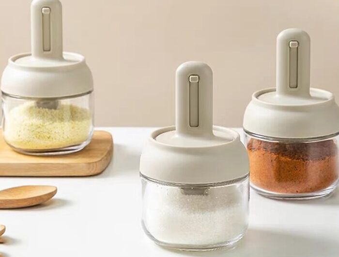 Set of three smart kitchen gadgets for spice storage with modern lids on a white countertop and wooden board.