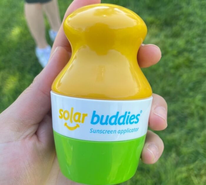 Hand holding a Solar Buddies sunscreen applicator outdoors on green grass, a warm weather find for easy sun protection.