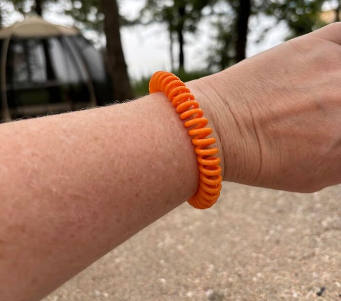 Close-up of a wrist wearing a bright orange coil bracelet as a warm weather find for thriving this season outdoors.