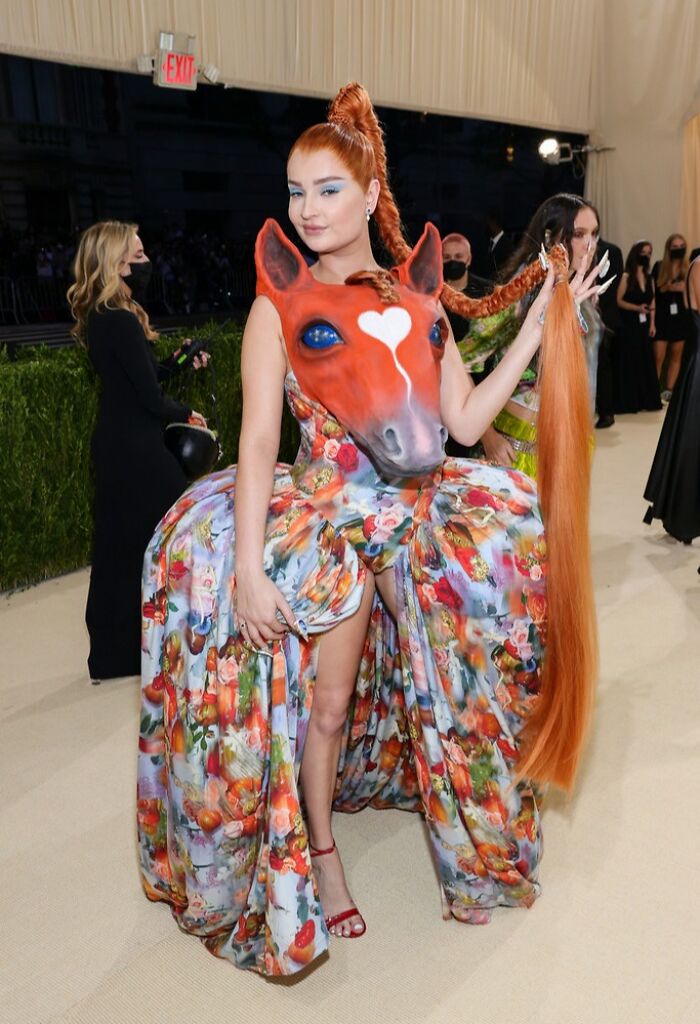 Woman at the Met Gala wearing an elaborate floral dress with a large horse head and long braided hair, showcasing failed fashion.