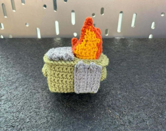 Crochet masterpiece of a small campfire with flames and a gray cloth on a textured surface.