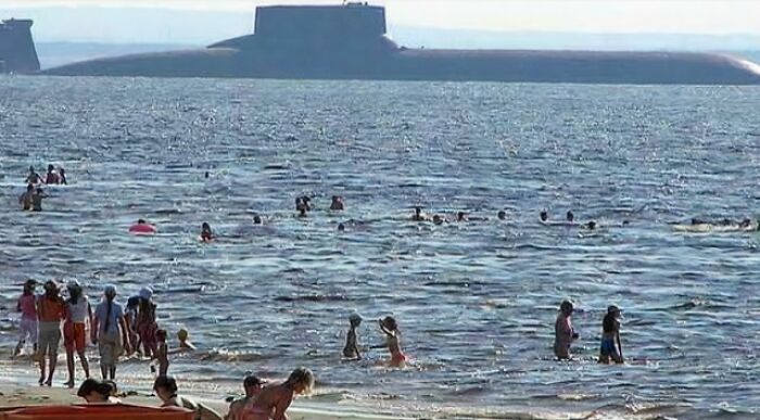 Large submarine in the ocean looms behind swimmers at the beach, illustrating a scarily big megalophobia scene.