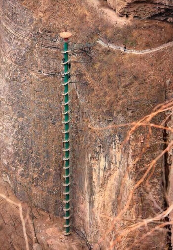Steep vertical ladder on rocky cliff with people climbing, illustrating a megalophobia fear of large heights.