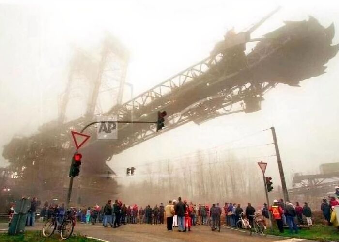 Crowd gathered near an enormous industrial machine towering over them, showing a scarily big structure causing megalophobia.