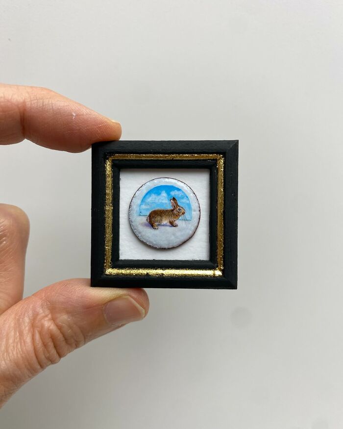 Hand holding a tiny one-inch painting of a rabbit against a plain background, showcasing detailed everyday art.