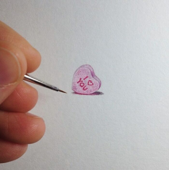 Tiny one-inch painting of a pink candy heart with I love you text being detailed with a fine brush.