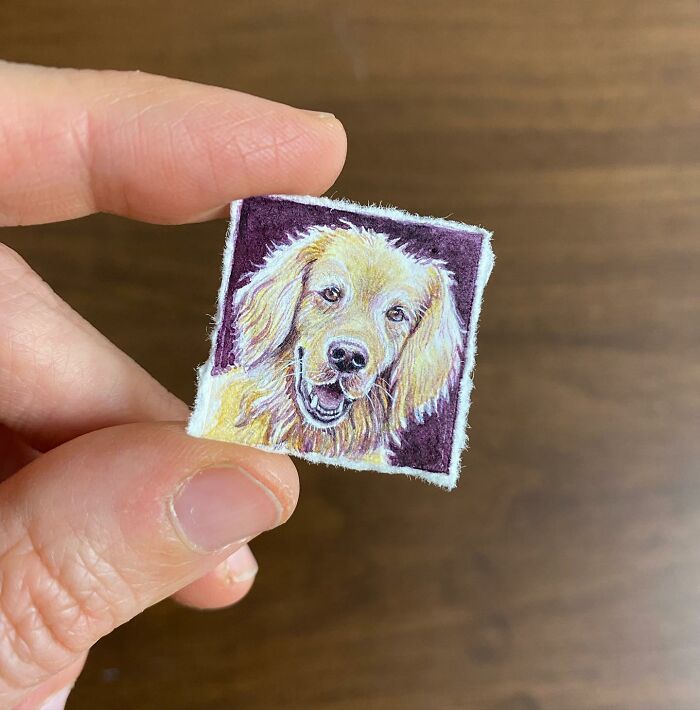 Hand holding a tiny one-inch painting of a golden retriever dog on a purple background by Brooke Rothshank.