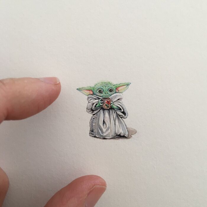 Tiny one-inch painting of Baby Yoda holding a cup, shown next to fingers for size comparison by Brooke Rothshank.