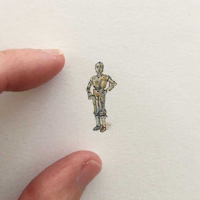 Tiny one-inch painting of a detailed robot figure held between two fingers on a white background.