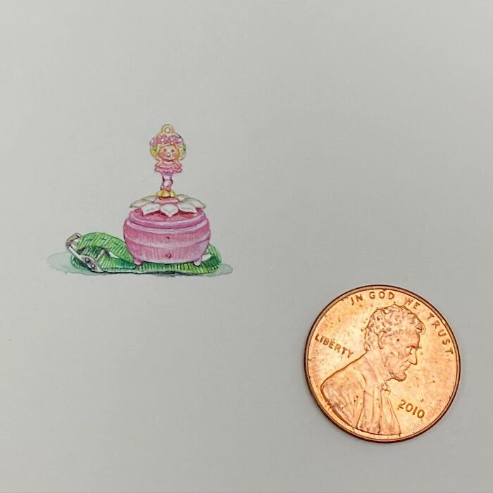 Tiny one-inch painting of a pink music box with a dancing figurine next to a US penny for size comparison.
