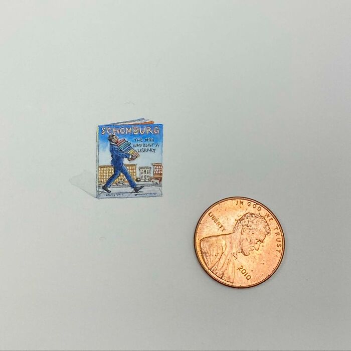 Tiny one-inch painting of a book by Brooke Rothshank shown next to a penny for size comparison.