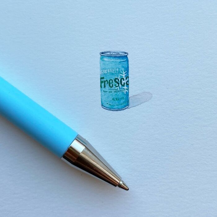 One-inch painting of a tiny soda can next to a blue pen, showcasing detailed miniature everyday art.