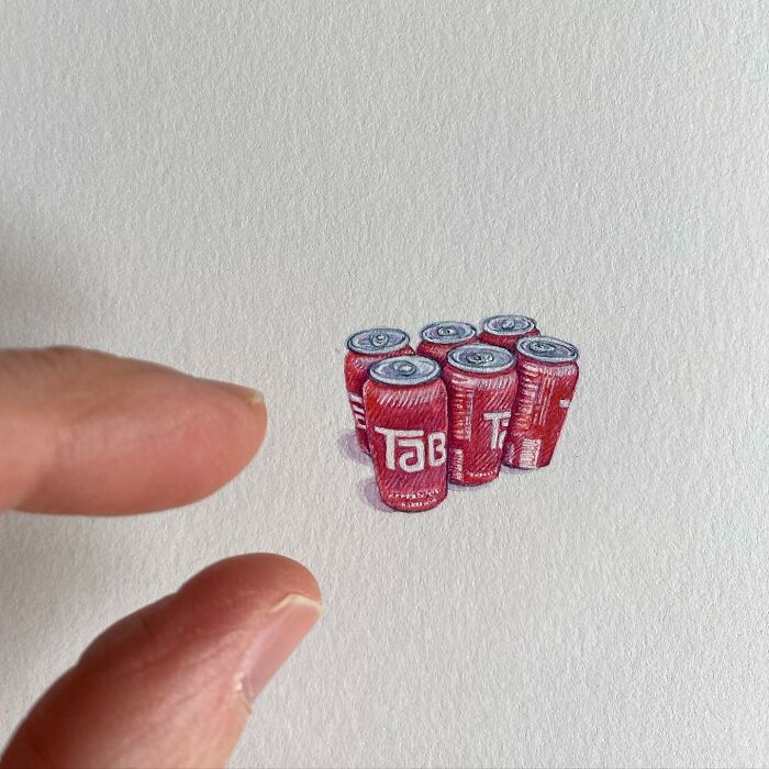 Tiny one-inch painting of a six-pack of red soda cans held between fingers by Brooke Rothshank.