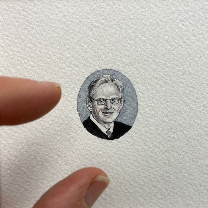 Tiny one-inch painting of a man with glasses on textured paper, shown between two fingers for scale by Brooke Rothshank.