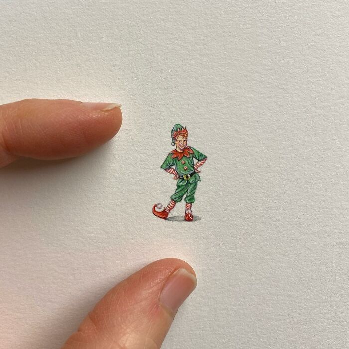 Tiny one-inch painting of a Christmas elf held between two fingers, showcasing detailed miniature art by Brooke Rothshank.