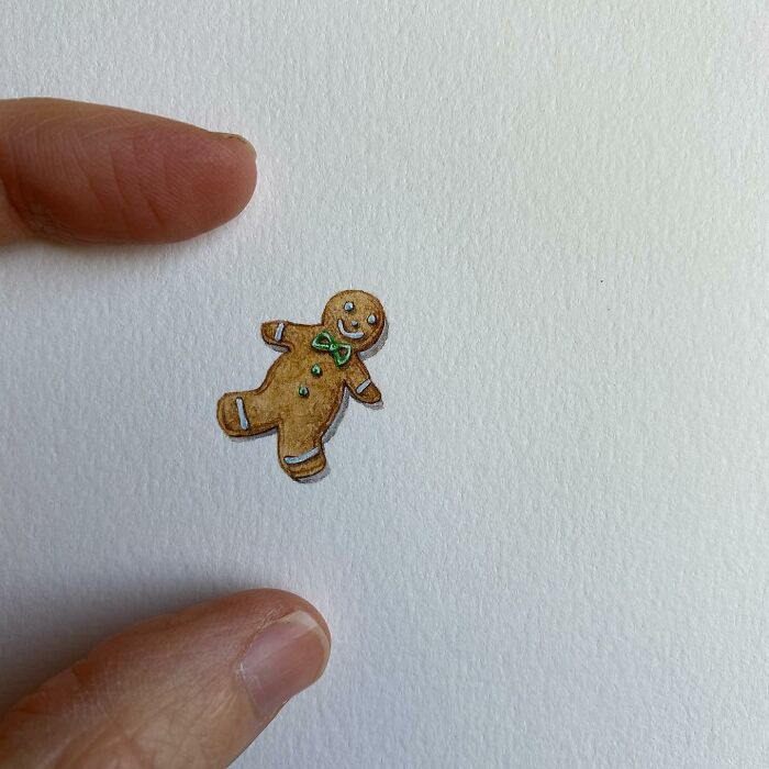 Tiny one-inch painting of a gingerbread man held between fingers showcasing everyday miniature art by Brooke Rothshank