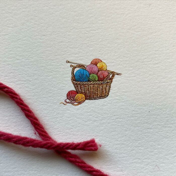 Tiny one-inch painting of colorful yarn balls in a woven basket with knitting needles by Brooke Rothshank