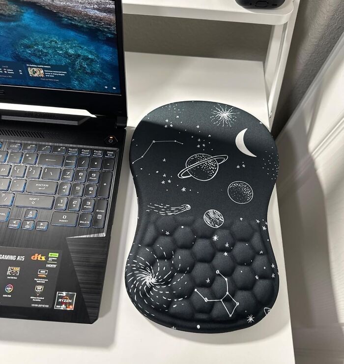Ergonomic mouse pad with space-themed design placed next to a gaming laptop as unique office supplies.