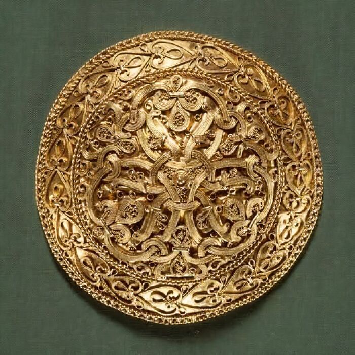 Intricately designed ancient gold artifact with detailed patterns displayed on a green background from archaeology news.