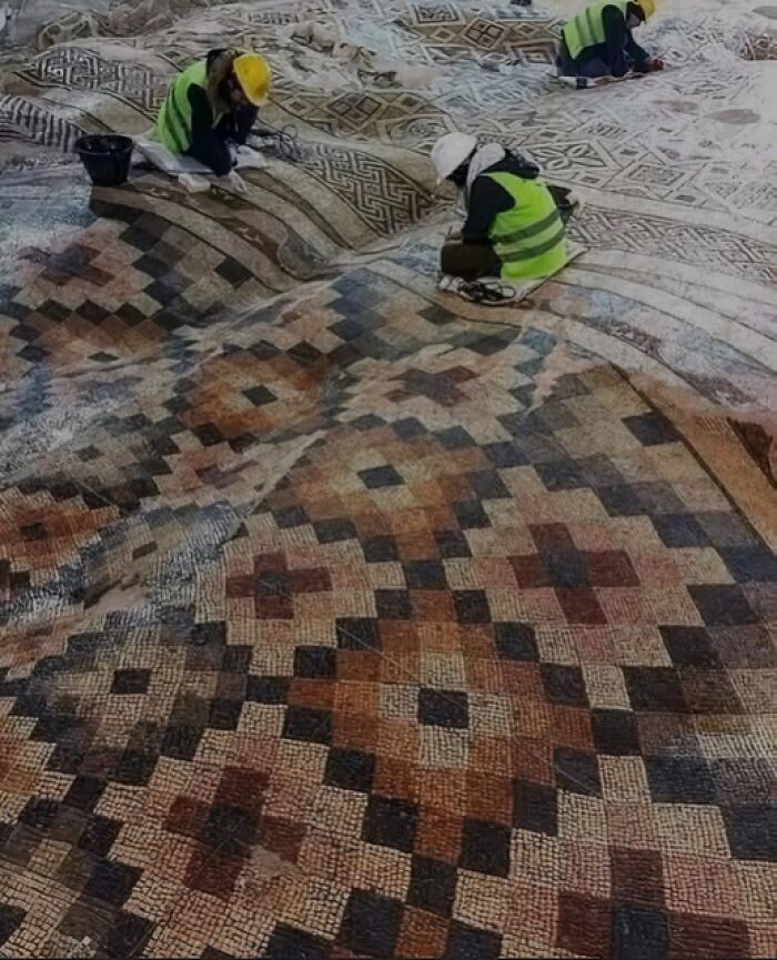 Workers carefully restore an ancient mosaic with geometric patterns, highlighting archaeology news and architectural preservation.