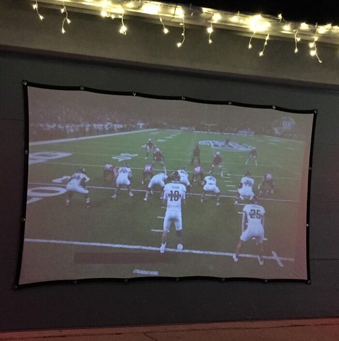 Outdoor projector screen displaying a football game with string lights, showcasing backyard outdoor upgrades for summer enjoyment.