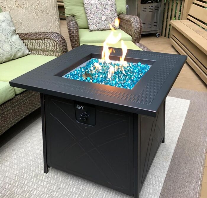 Modern outdoor fire pit with blue glass rocks surrounded by cushioned wicker seating in a backyard upgrade setting