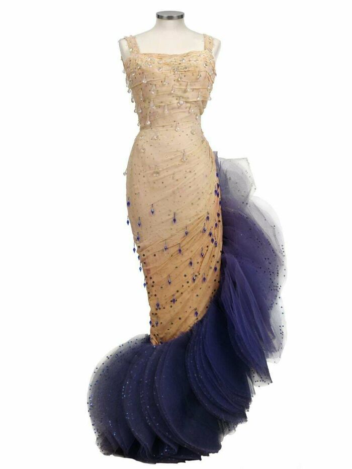 Beige and navy blue evening gown with intricate beadwork and layered tulle, showcasing centuries of fashion evolution.