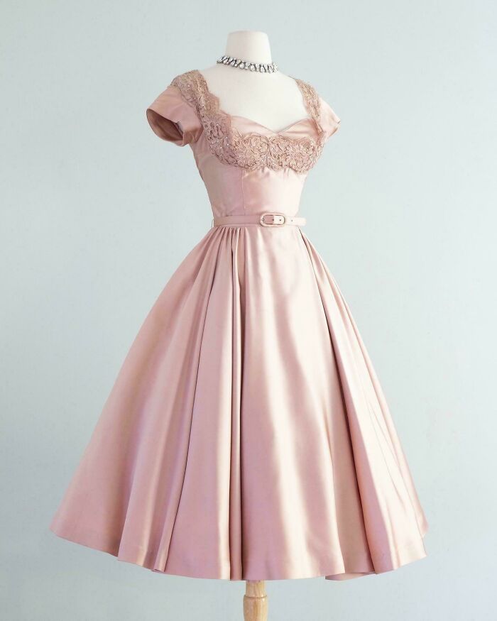 Vintage pink satin dress with lace details and belt displayed on a mannequin, showcasing centuries of fashion history.