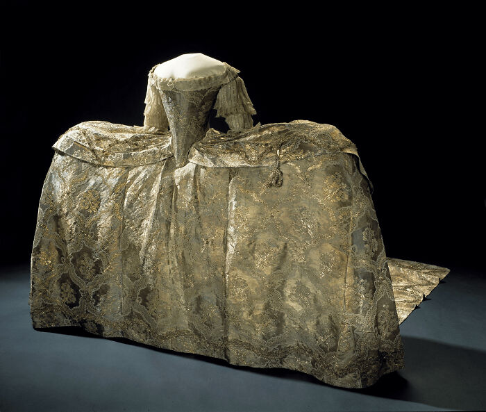 Elaborate historic dress with wide silhouette and intricate gold embroidery showcasing centuries of fashion evolution.